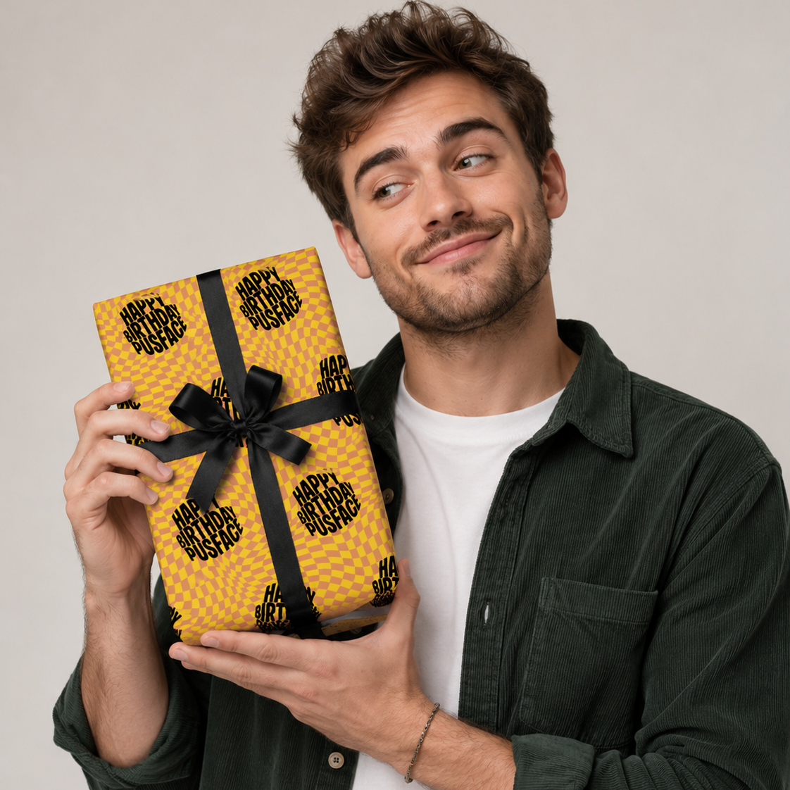 Man holding a gift wrapped in Happy Birthday Pusface wrapping paper with a black ribbon, smiling with a playful expression.